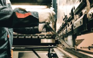 A person in gloves forming metal in a machine in El Paso.